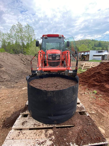 Tractor filling a large fabric pot with soil at the farm.