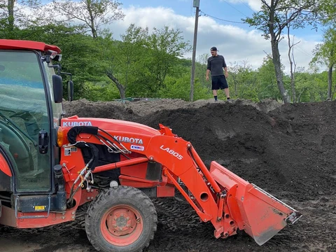 Red Kubota tractor moving soil at Bone Creek Farm.
