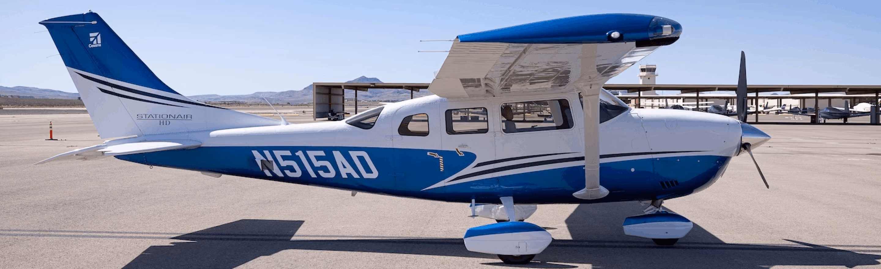 Blue and white single-engine airplane parked on a sunny airport tarmac.