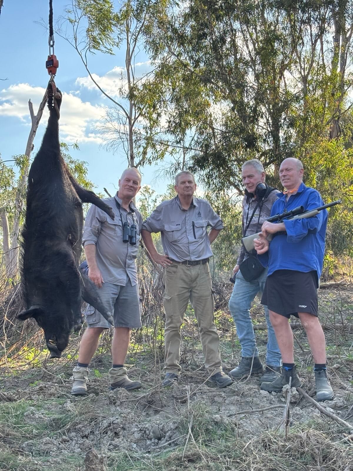 Four hunters standing beside a wild boar hung from a tree