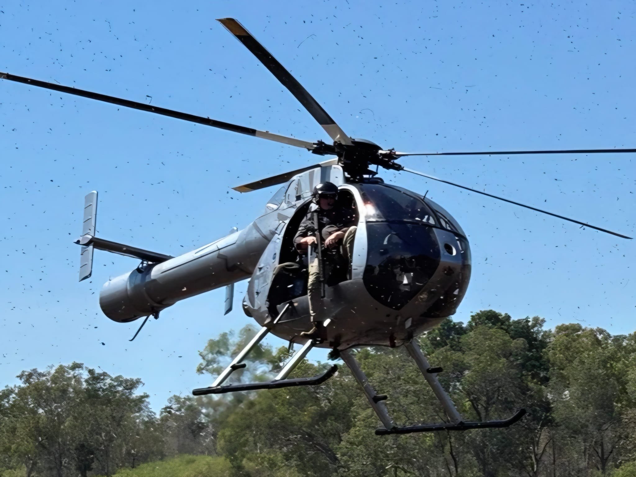 A helicopter approaching to land in the bush with a hunter sitting in the open door