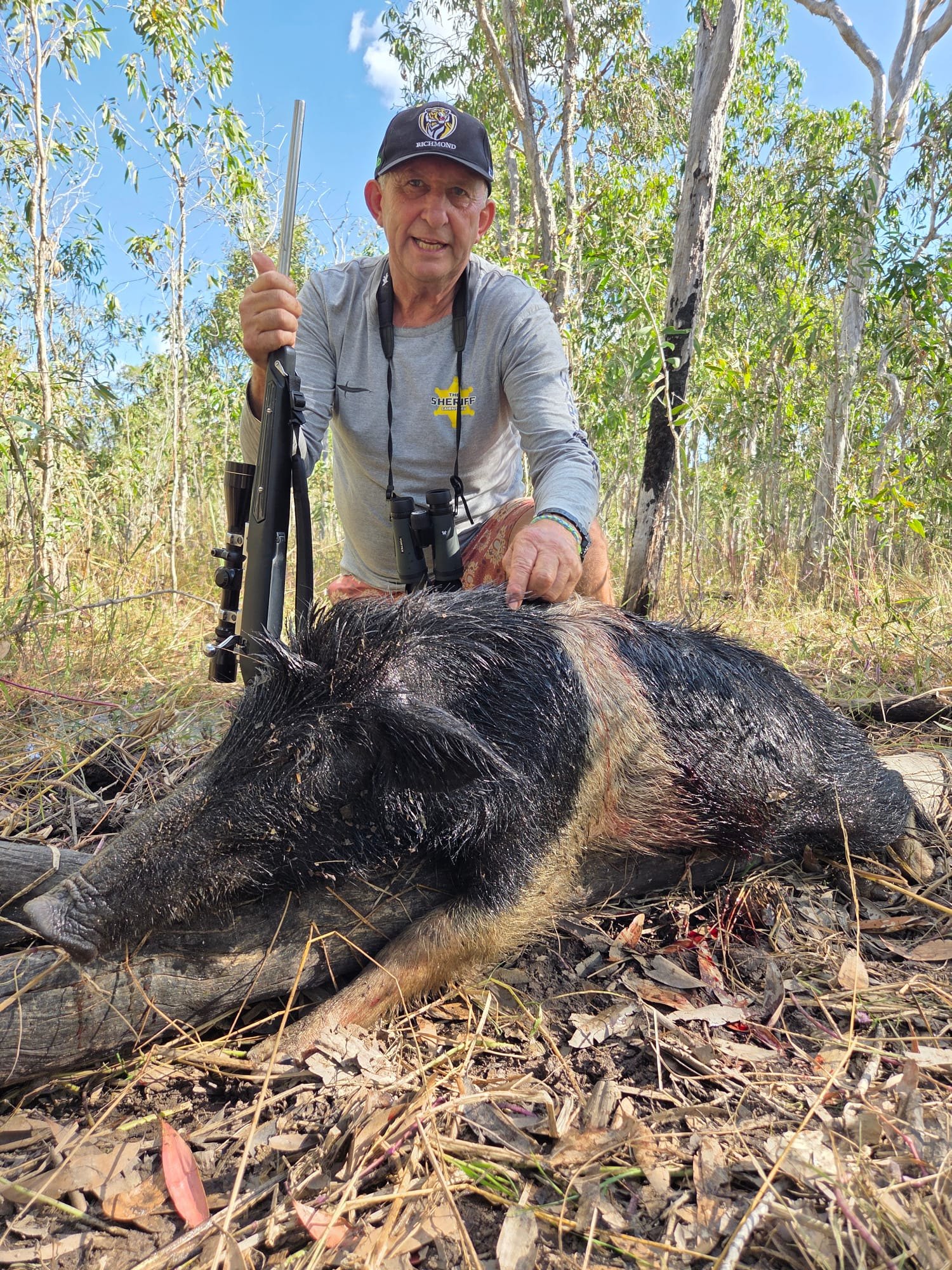 A hunter crouching with a rifle beside a black boar with a pale band across its shoulders
