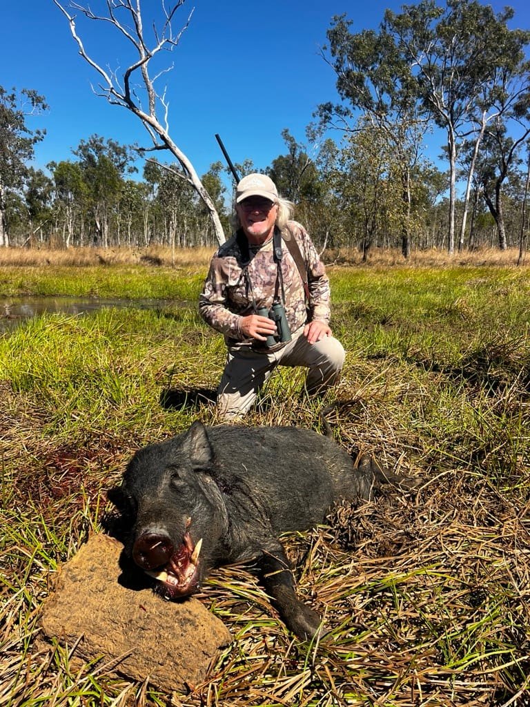 A hunter kneeling beside a small wild boar resting on a termite mound