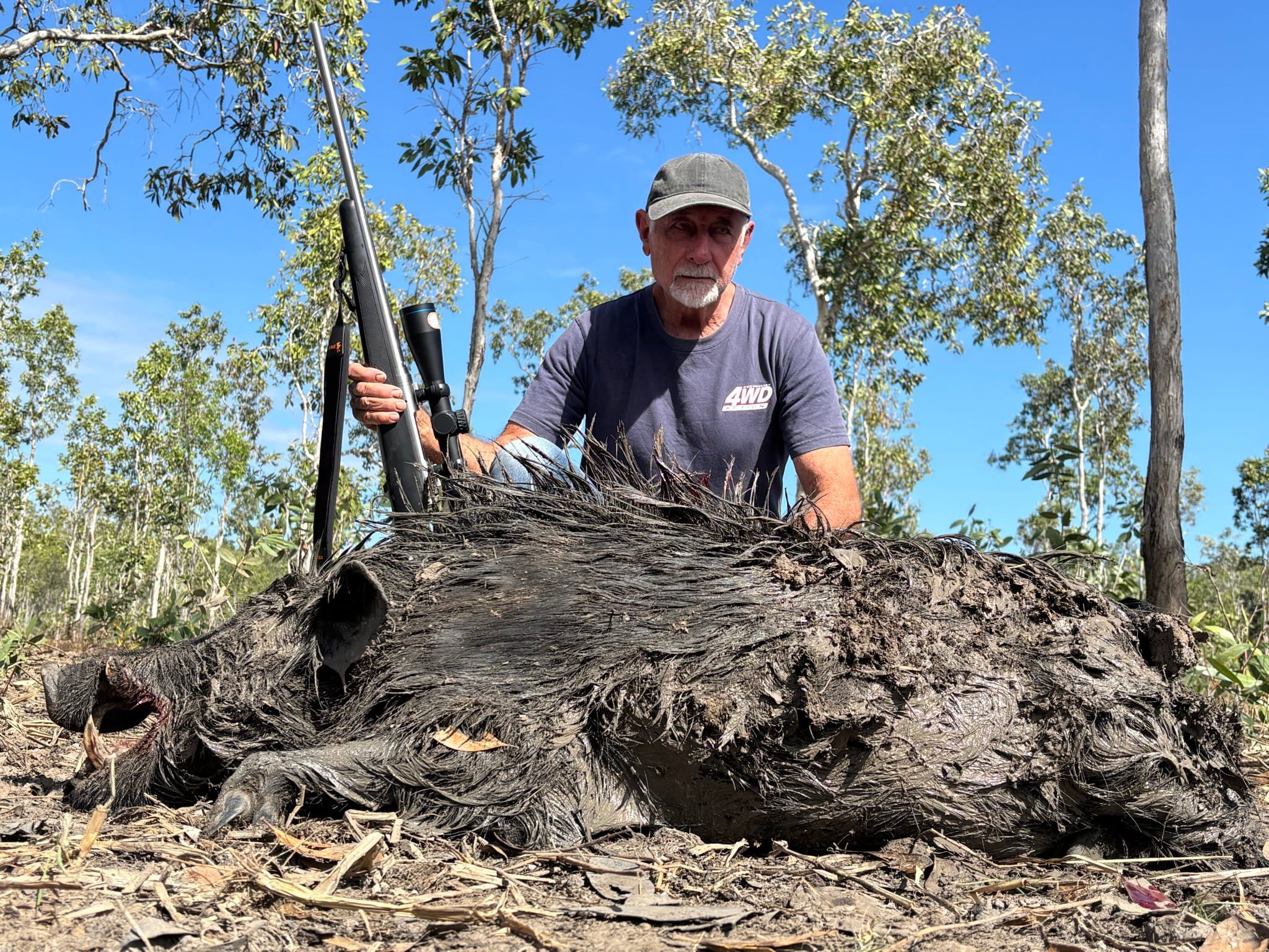 A hunter in a cap behind a large wild boar with a rifle upright beside it