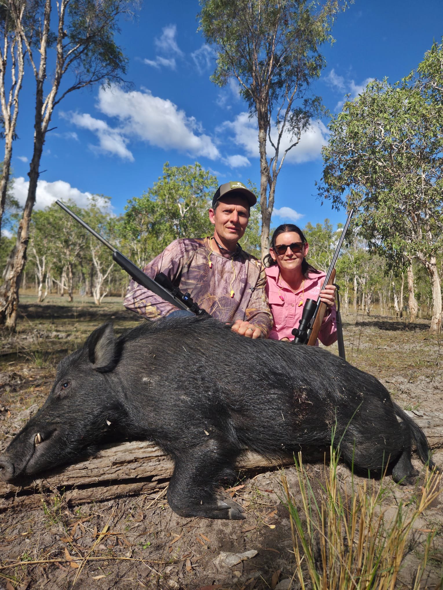 Two hunters crouching behind a wild boar in open forest