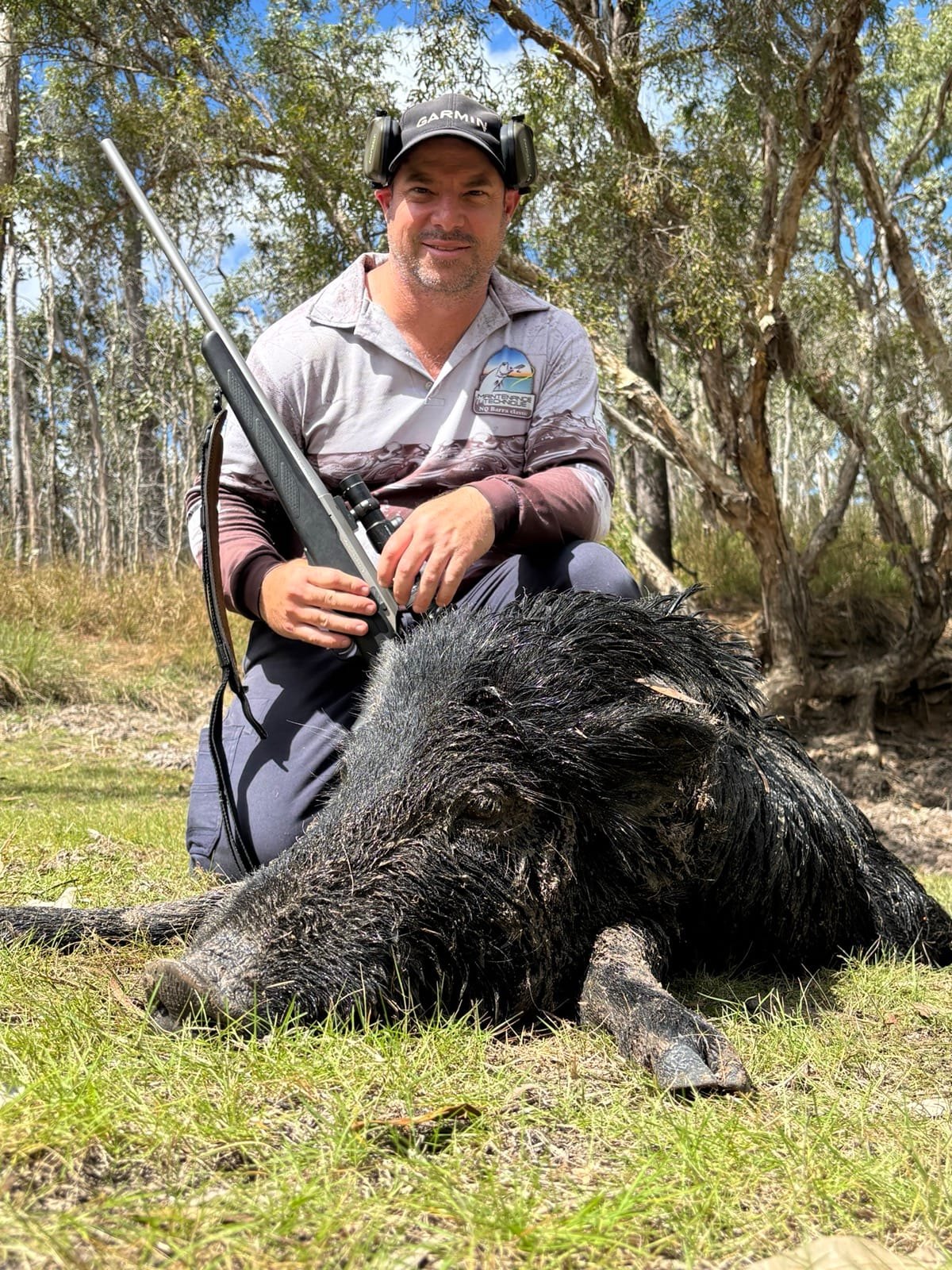 A hunter crouching with a rifle beside a large wild boar on green grass