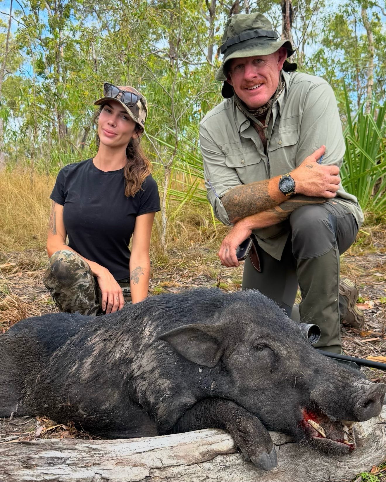 Two hunters crouching behind a wild boar beside a log