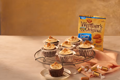 Cupcakes with creamy toffee frosting on a wire rack with Werther's Original candies in background.