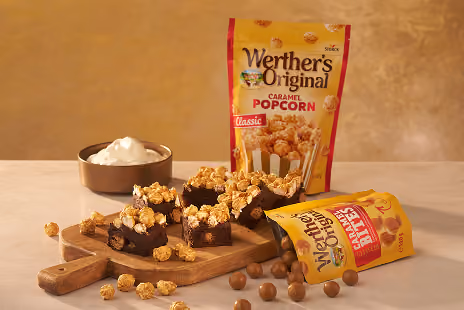 Werther's caramel popcorn with chocolate squares topped with popcorn and caramel balls on a table.