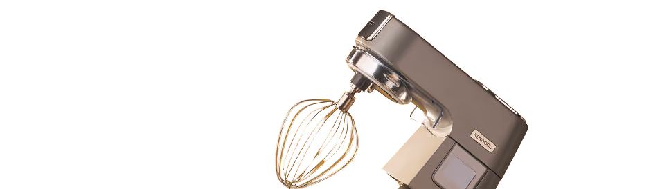 Kenwood stand mixer with a gold-colored wire whisk attachment on a transparent background.
