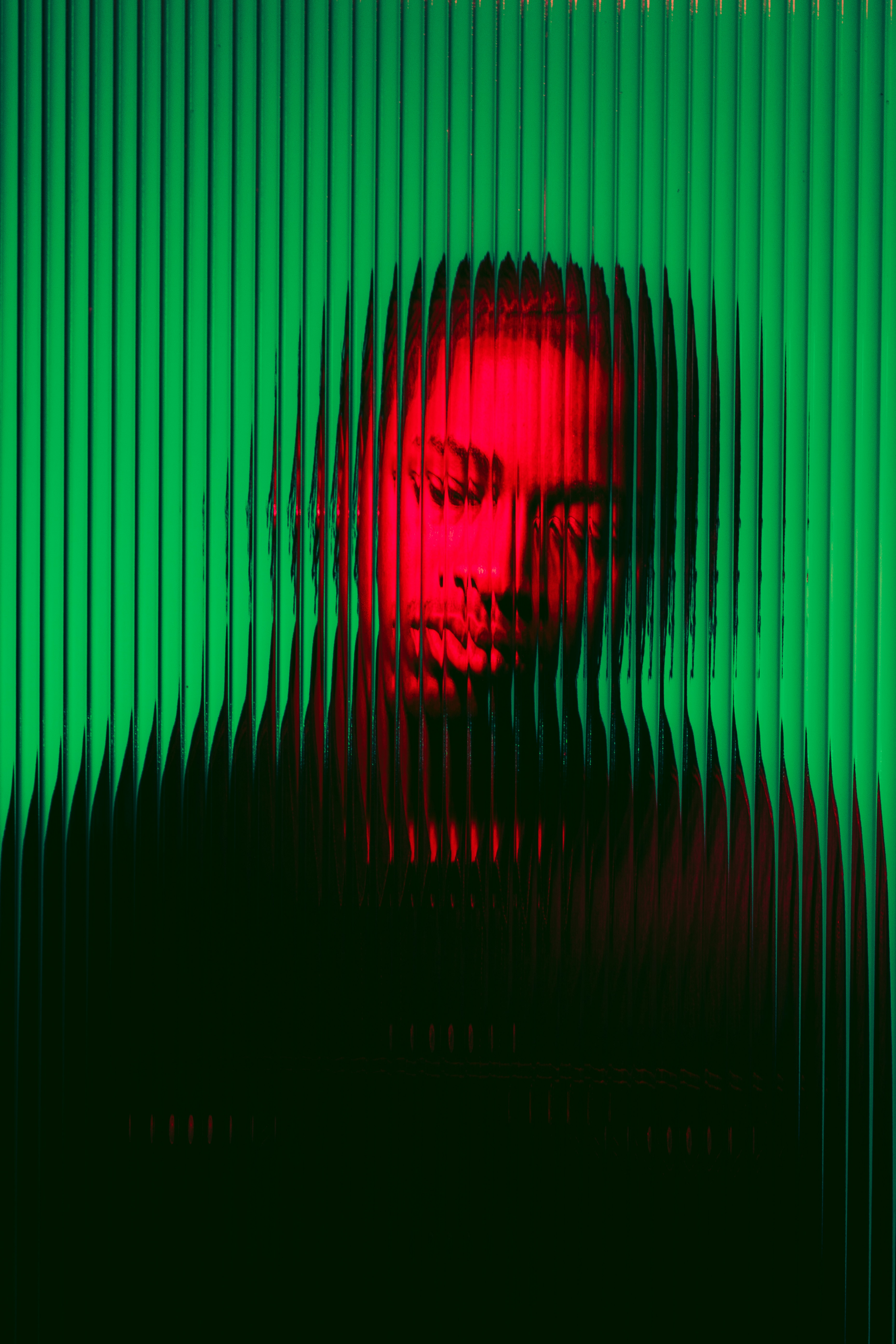 Portrait of a man distorted by vertical glass ridges lit red against a green background.