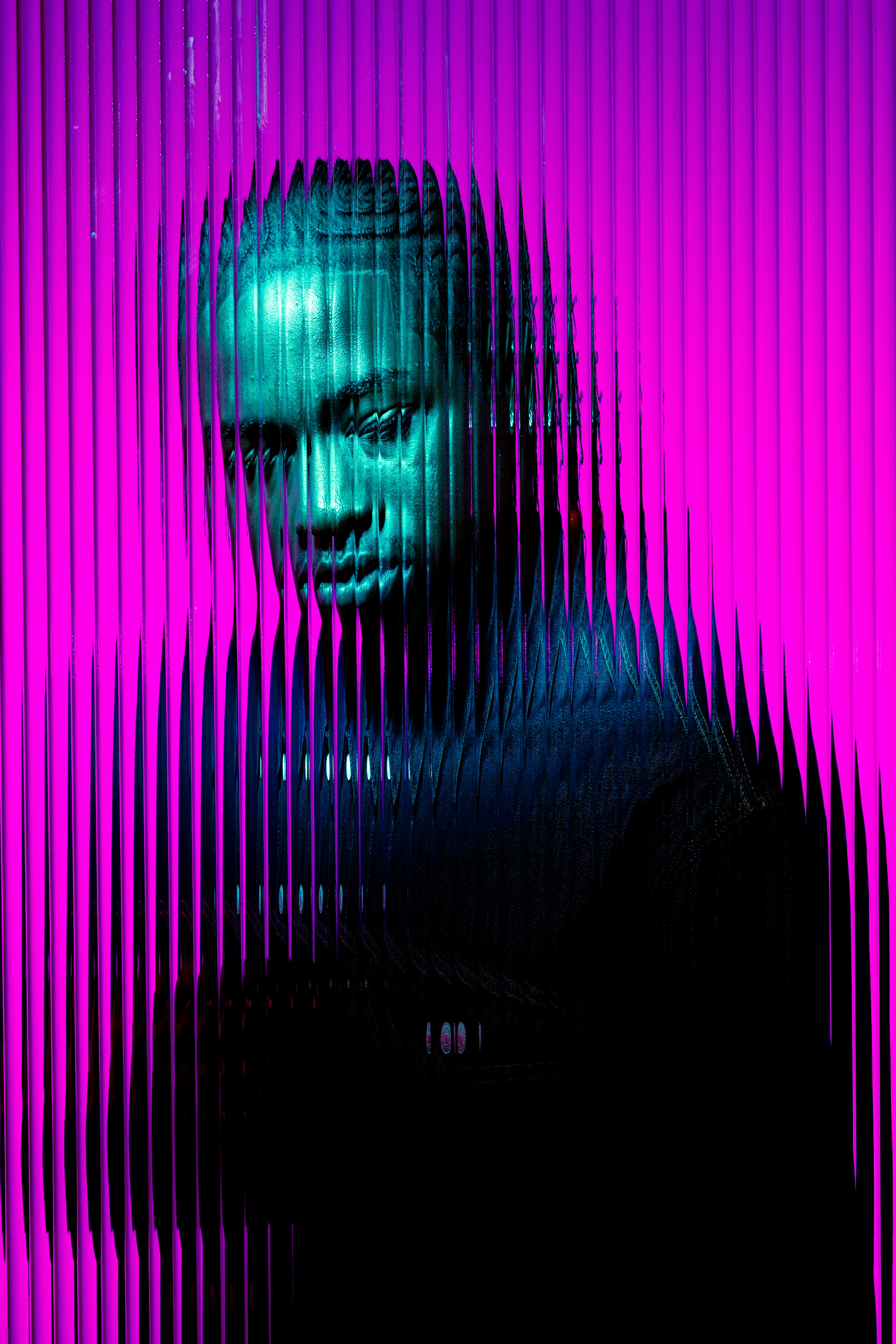 Portrait of a man with braided hair viewed through vertical textured glass with neon purple and blue lighting.