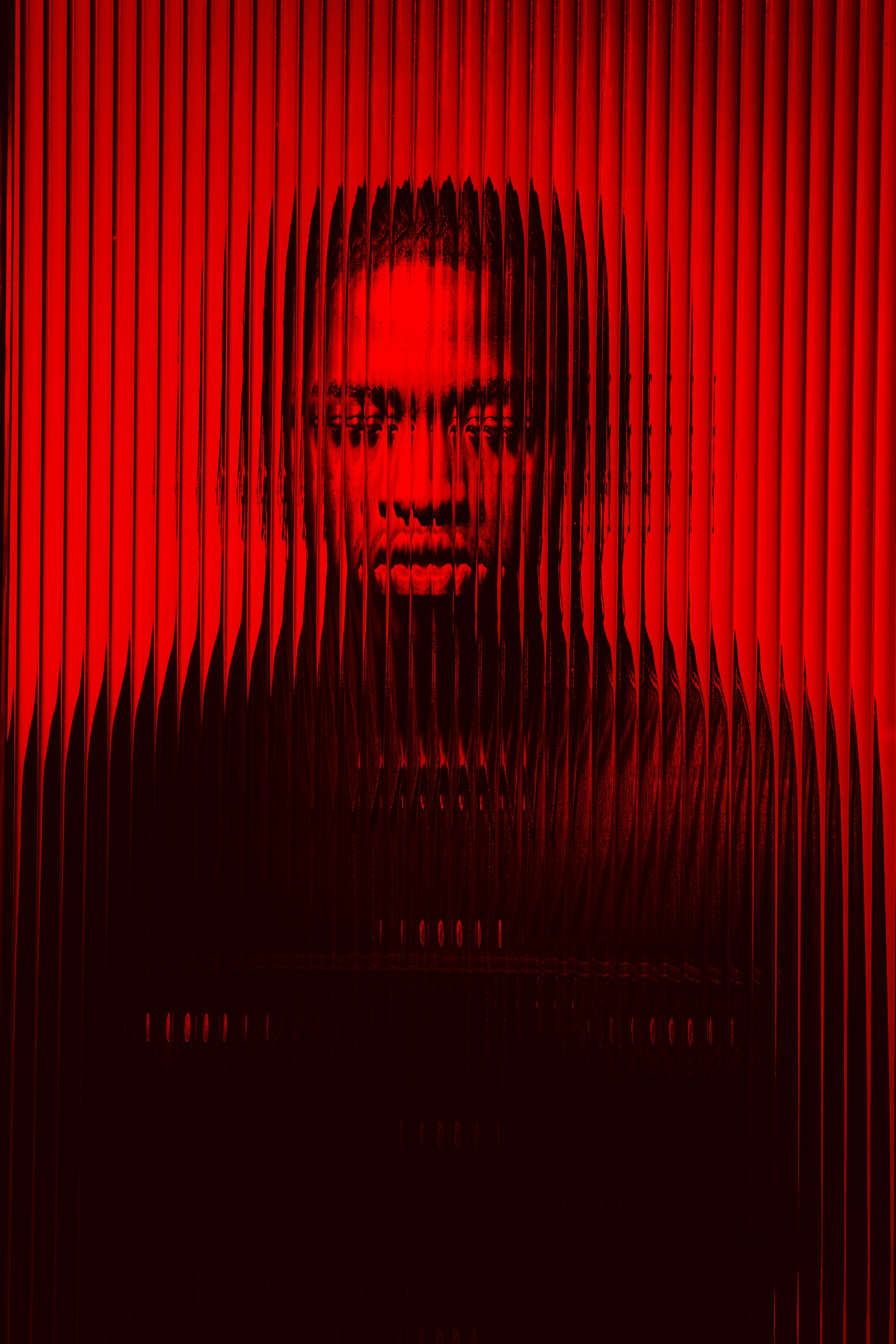 Portrait of a man distorted by vertical red translucent glass panels.