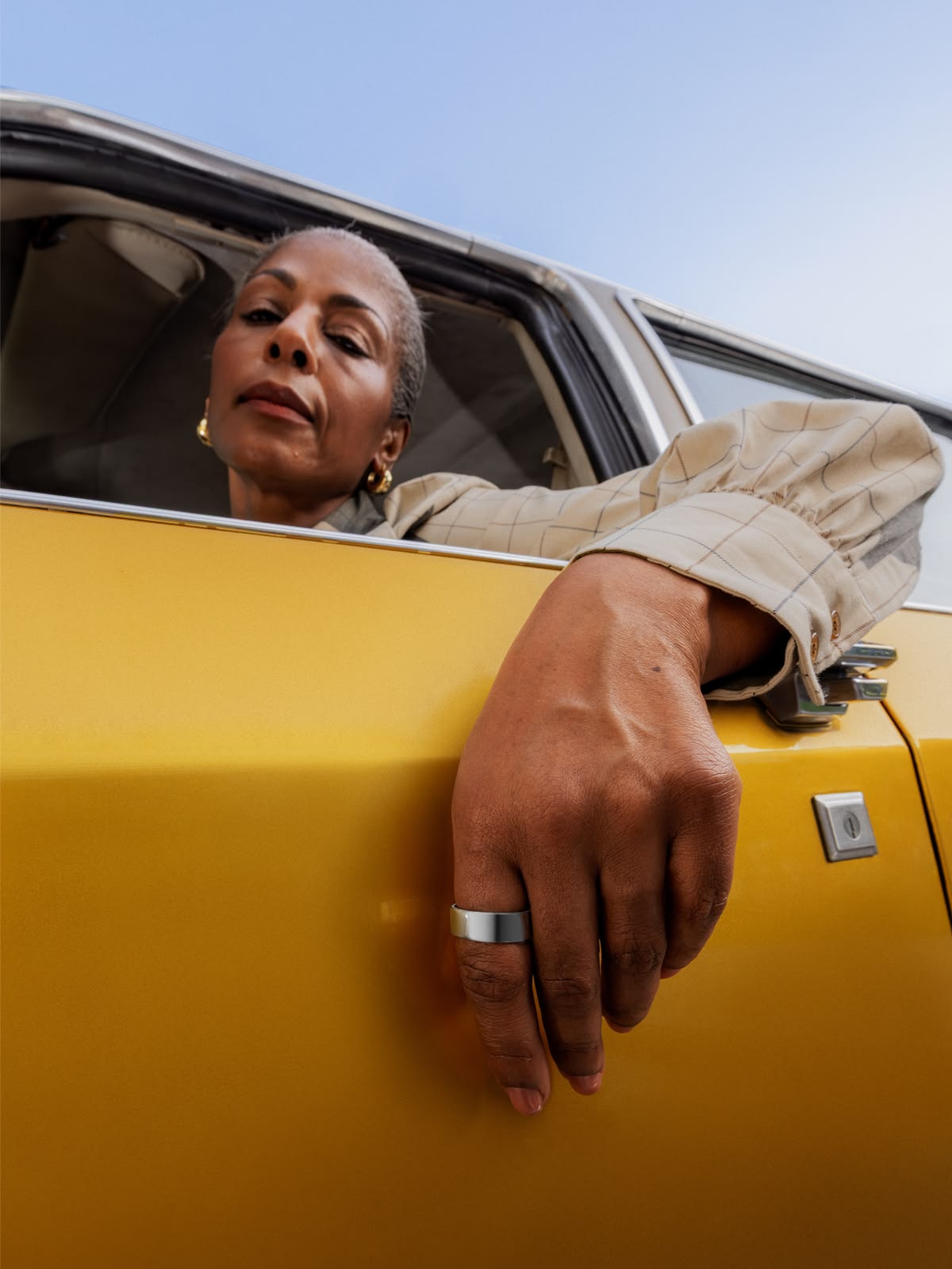 Woman with braided hair wearing translucent orange sunglasses and a beige sweater indoors.