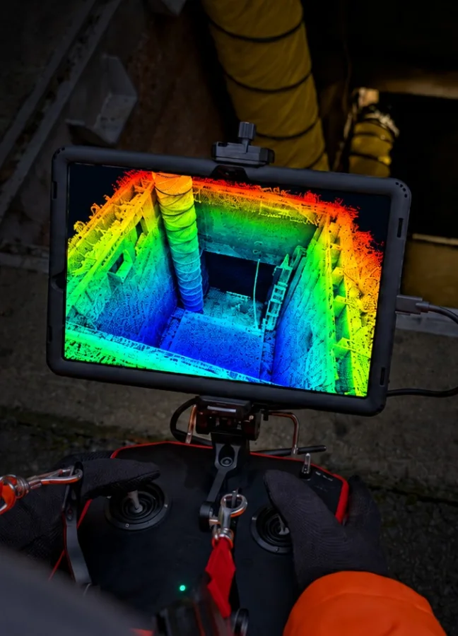 Fernsteuerung mit Tablet über einem offenen Schacht, auf dem Bildschirm die farbige LiDAR-Punktwolke des Schachts