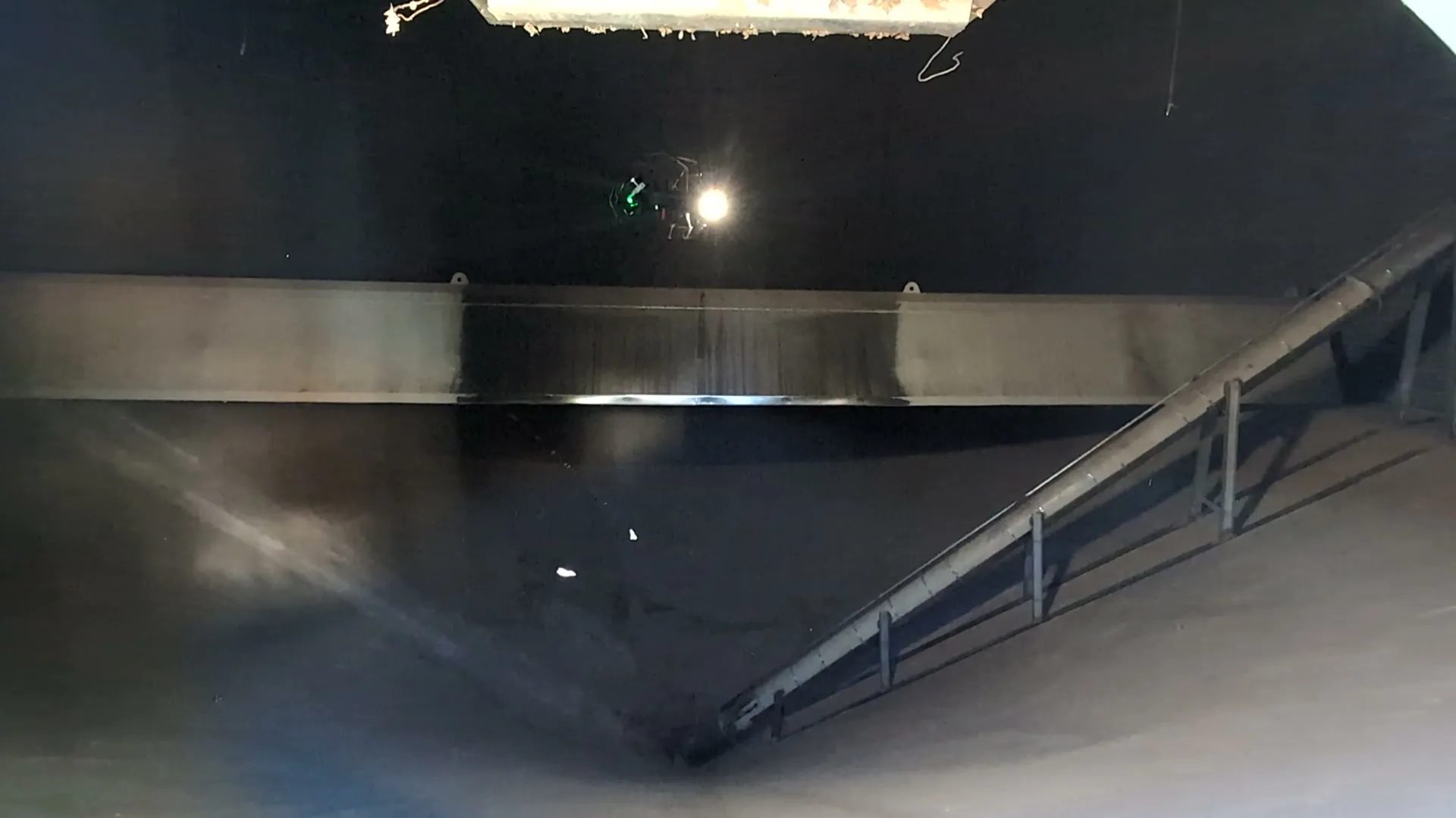 Inspektionsdrohne mit Scheinwerfer und grünem Licht fliegt im dunklen Silo unter der Decke