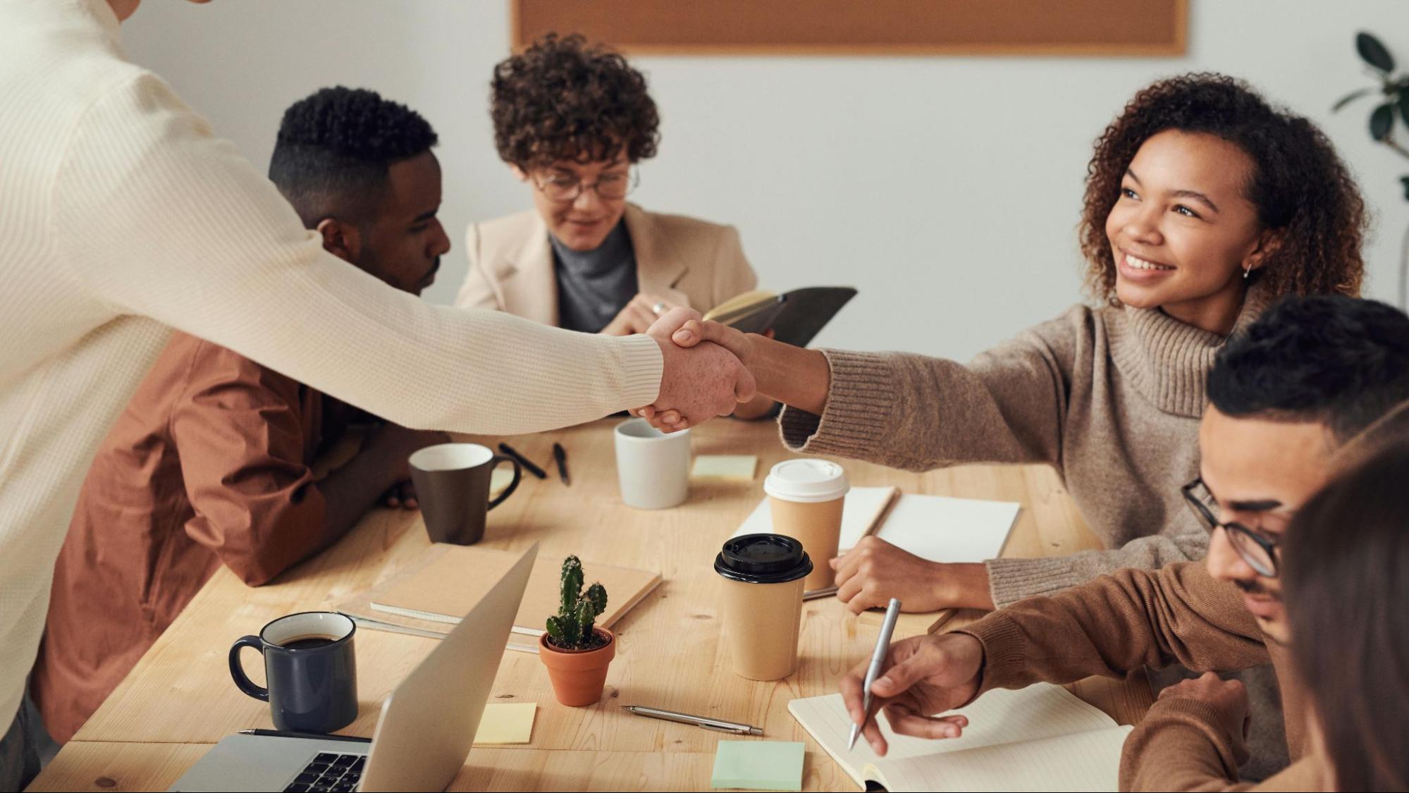 An image of a team having a meeting, with two of the people shaking hands while preparing offboarding.