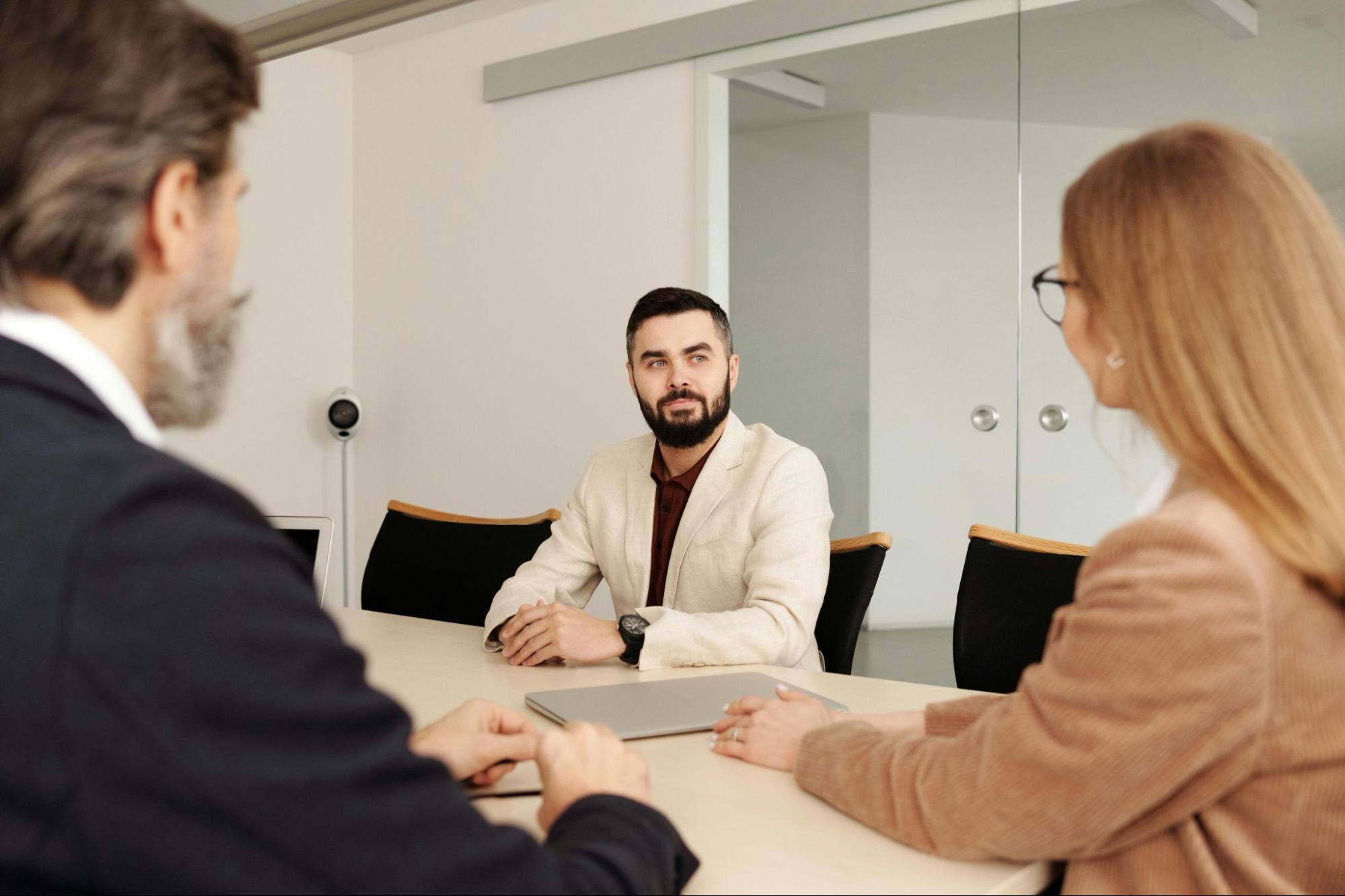 Two HR team members sit at a table facing an employee in a meeting room.