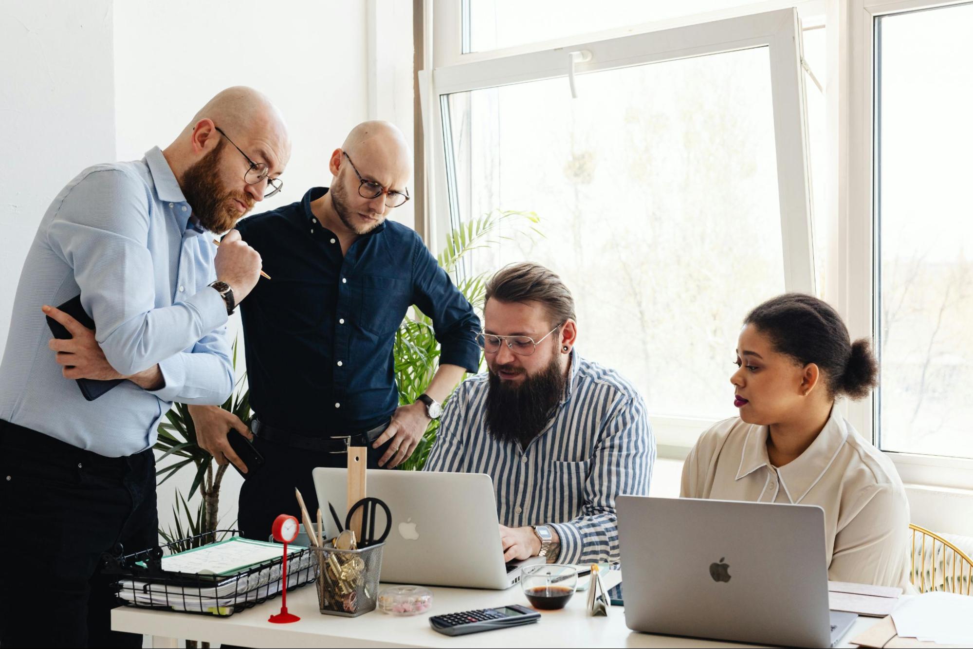 Four employees gathered around a table looking at a laptop.