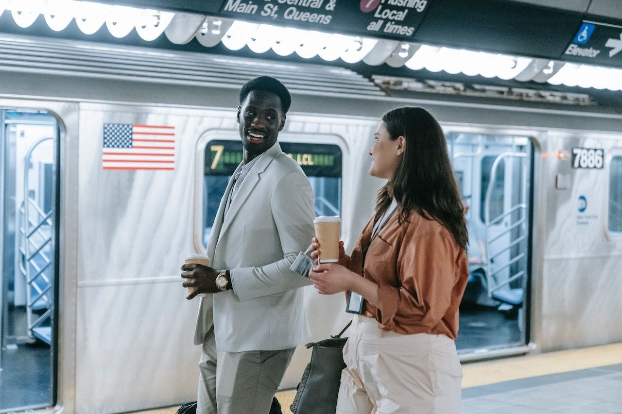Two employees carrying coffee cups and talking in front of a New York City subway car.