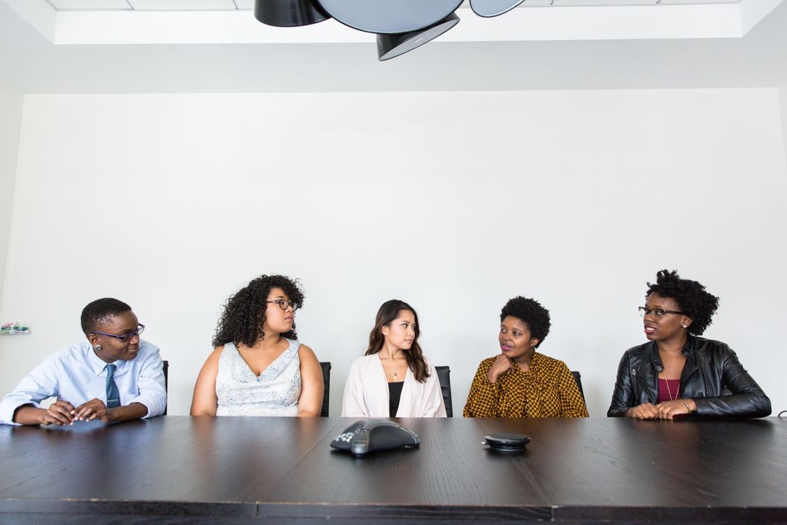 Five people at a desk with a speakerphone, having a conversation.