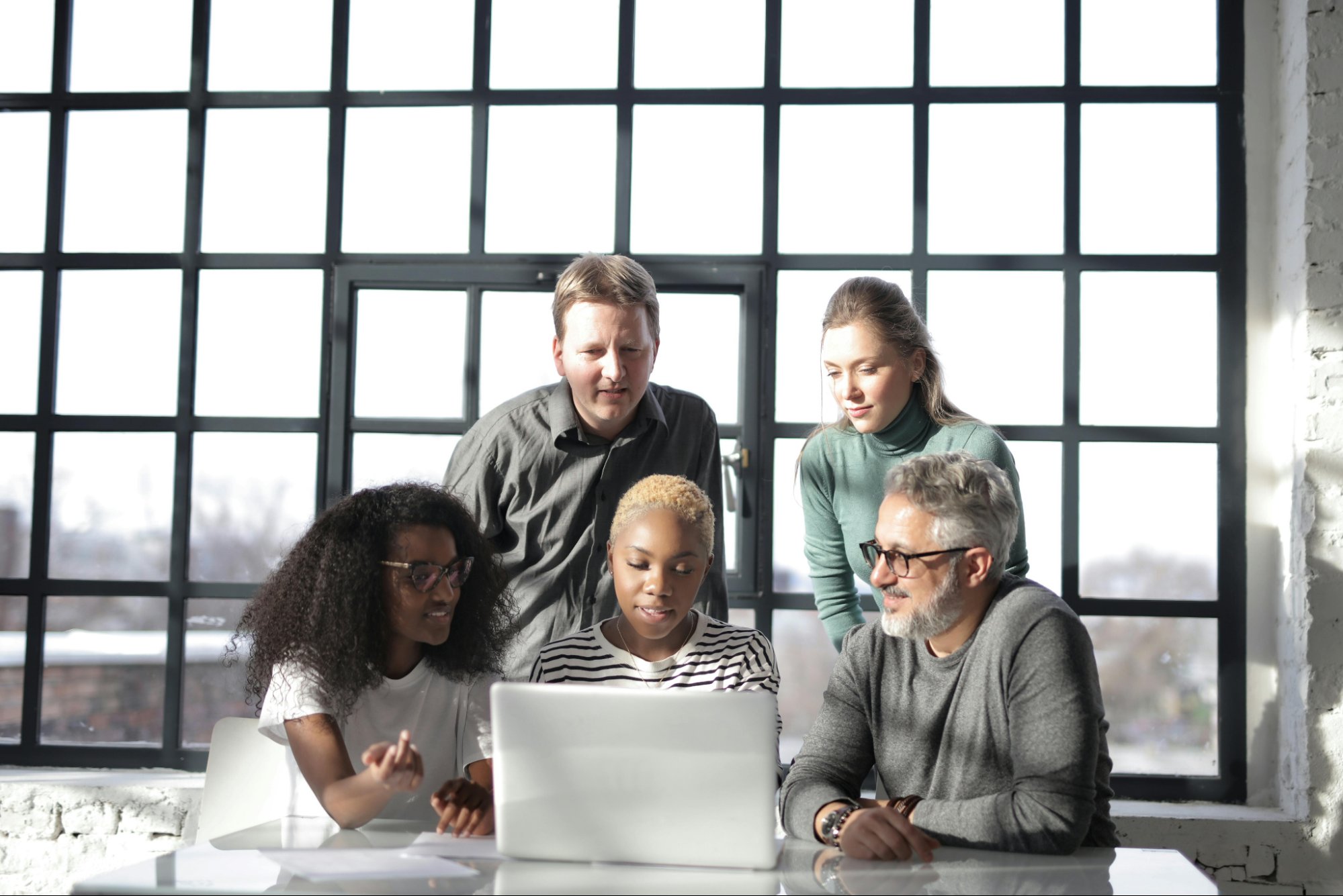 Five people behind a large paneled window at a table looking at a laptop screen.