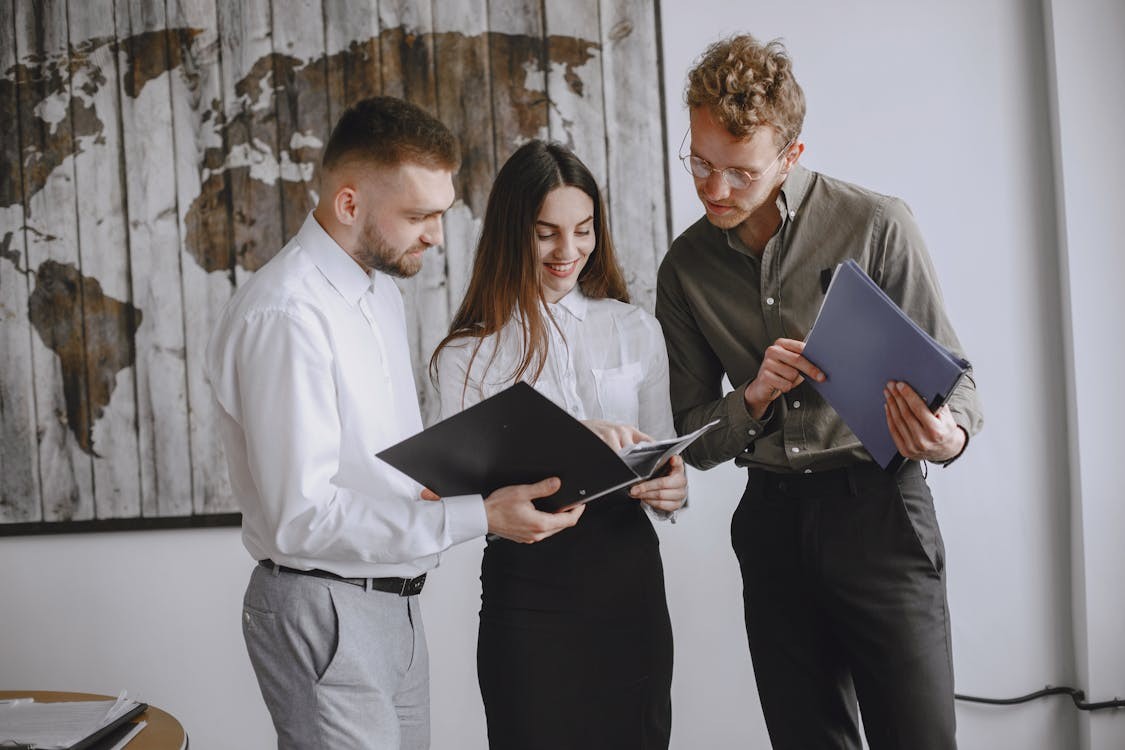 Three office workers review a folder of documents together.