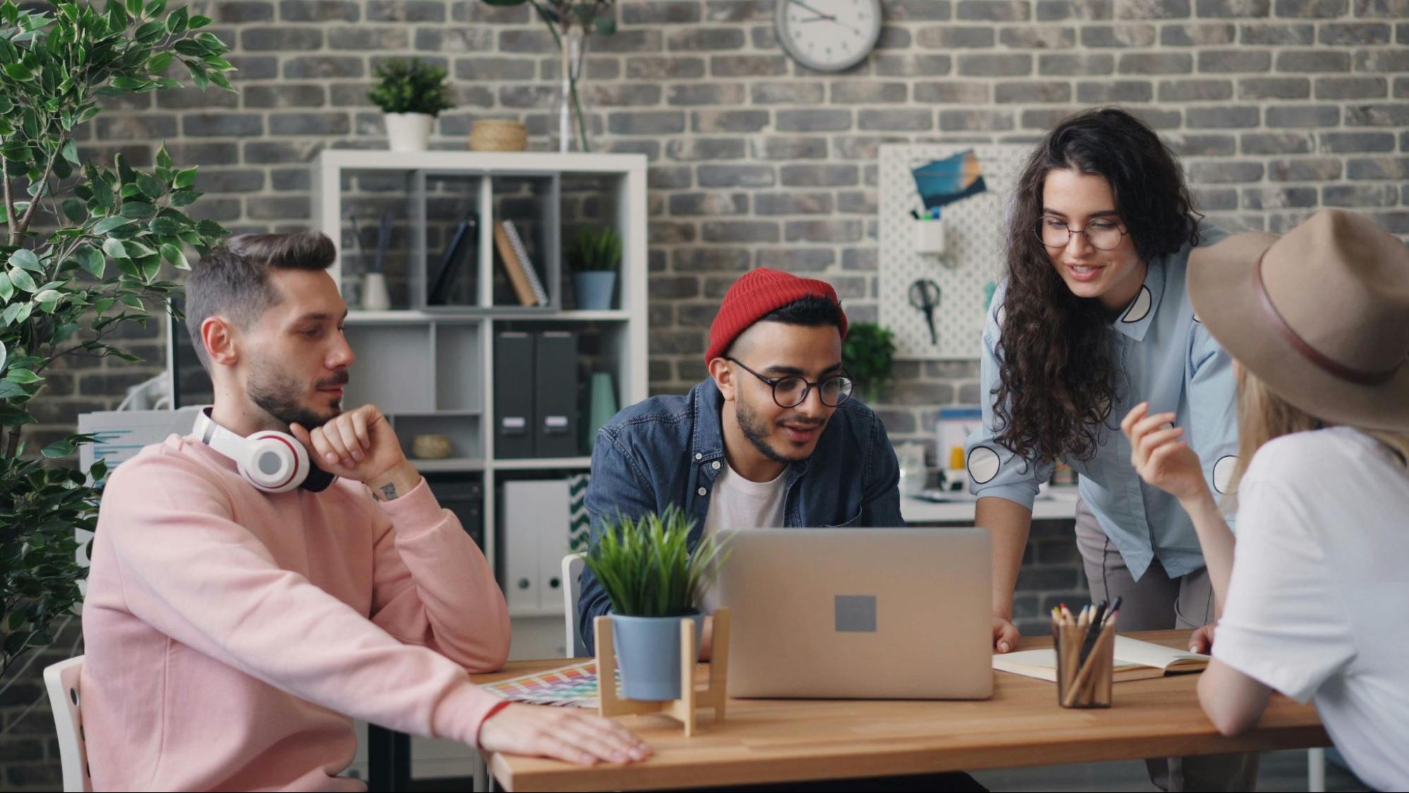 Four people working together over a desk and laptop.