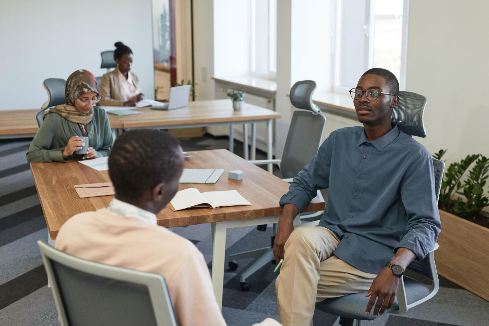 Two employees reading paperwork at tables, while two other people sit facing one another.