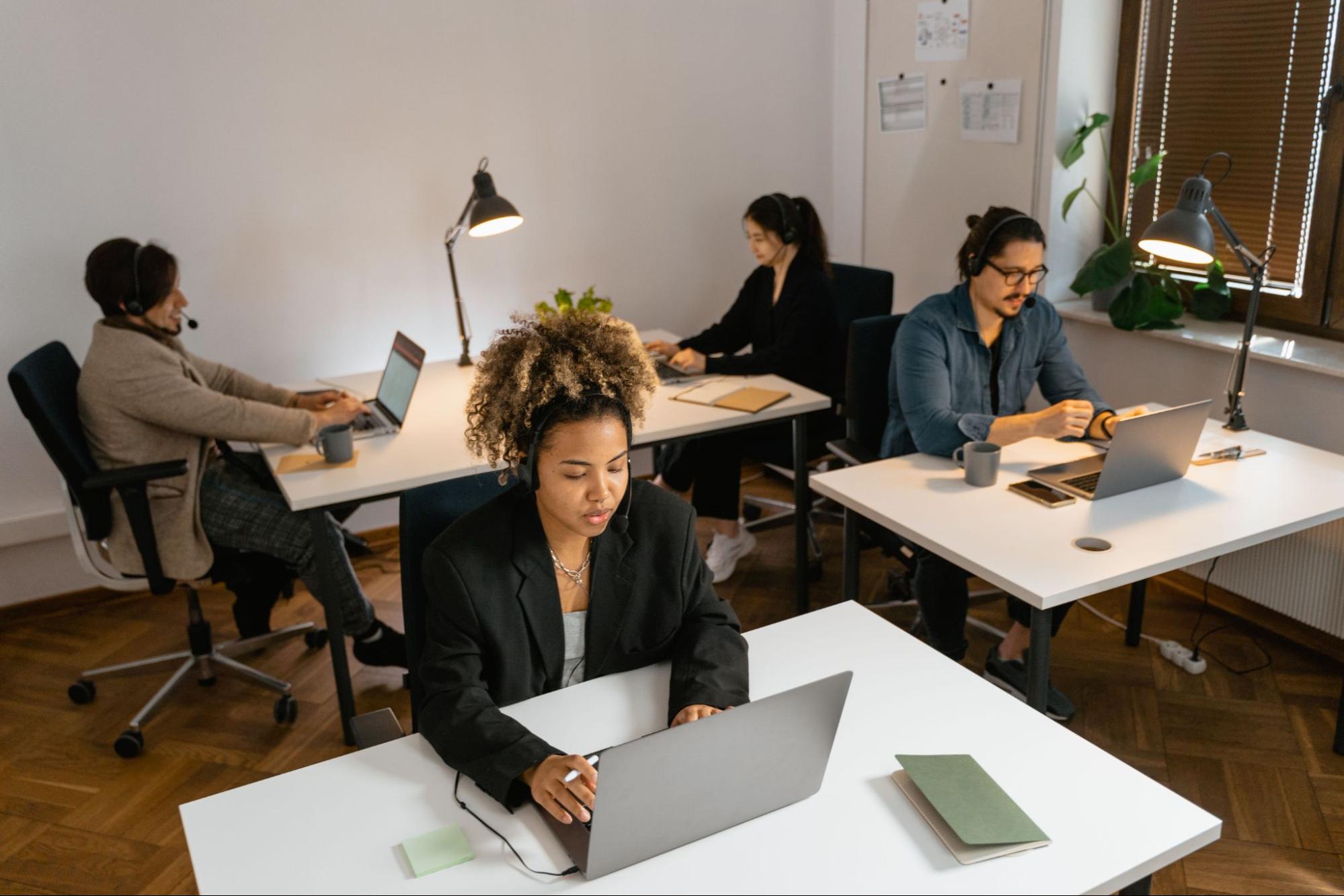 A group of four professionals working on laptops at desks in an office.
