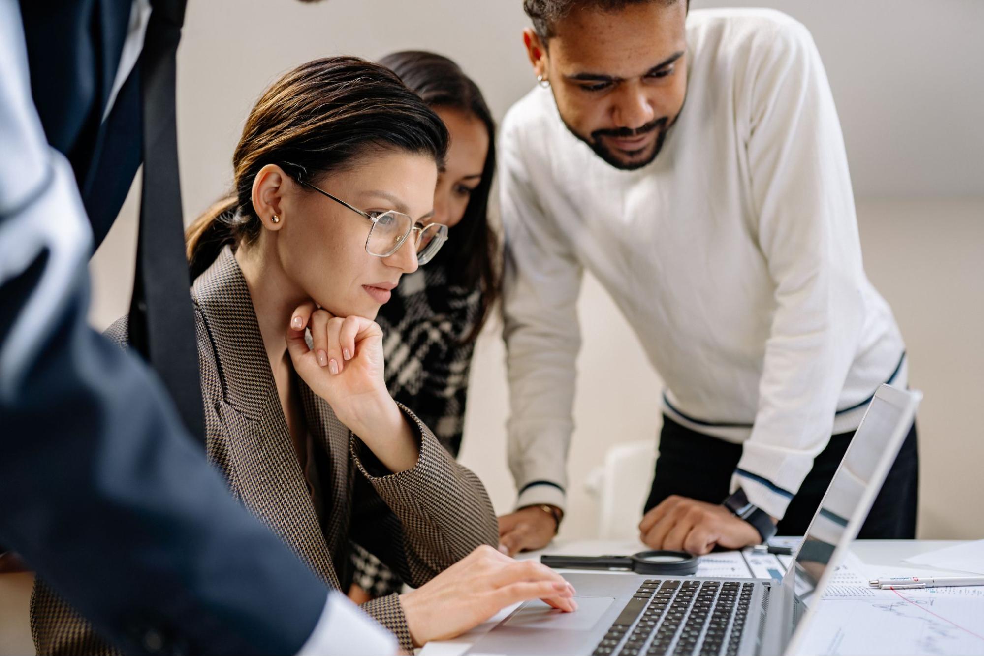A group of four people working together over a laptop at a desk.