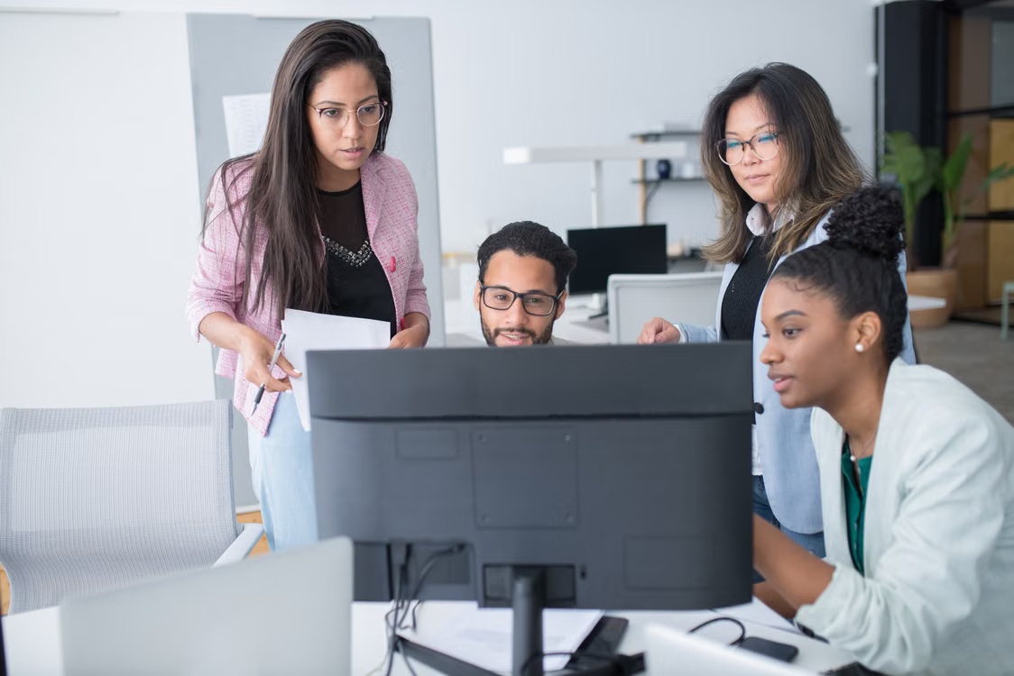 Four office workers having a discussion around a desktop computer.