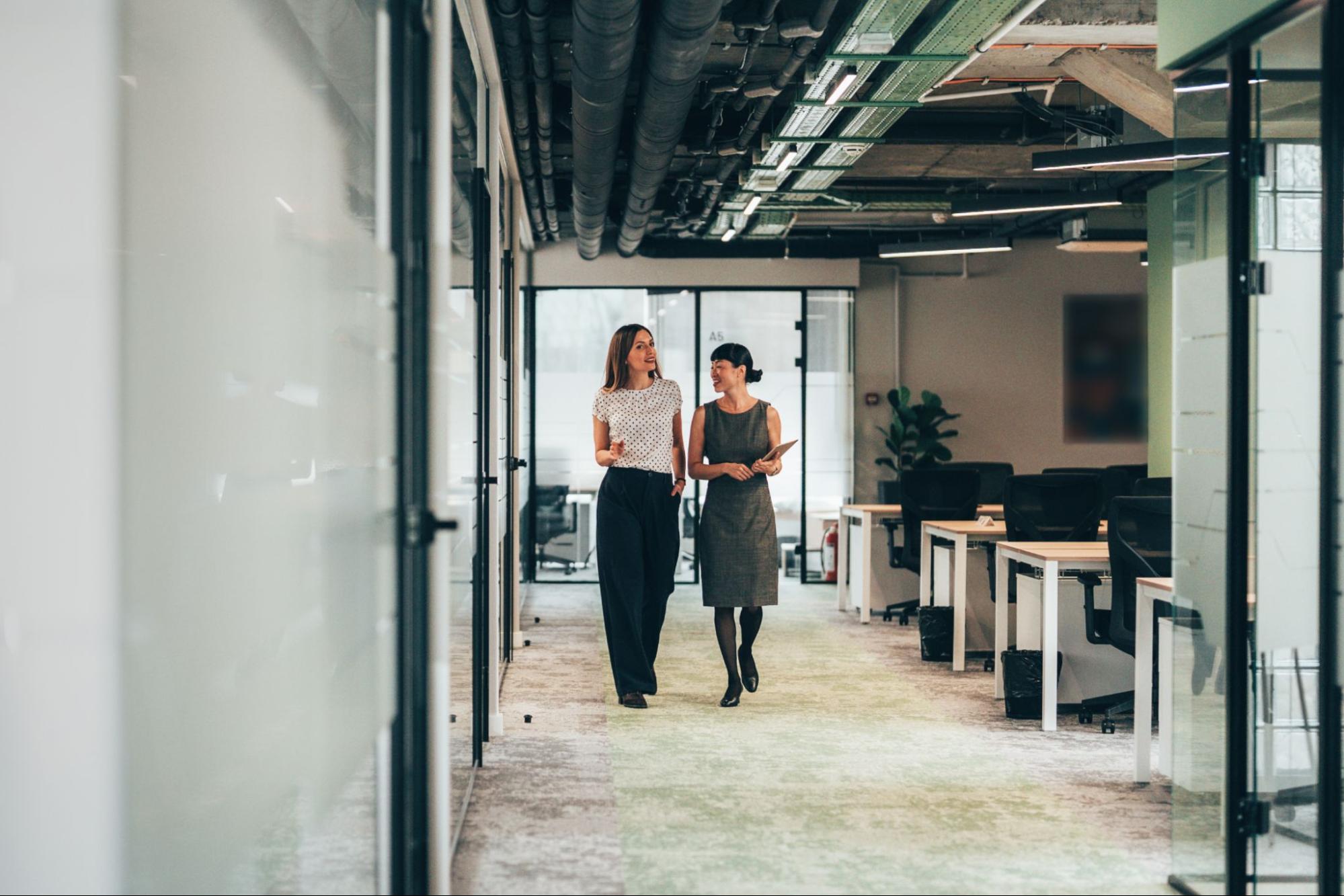 Two colleagues walking and talking in an office.