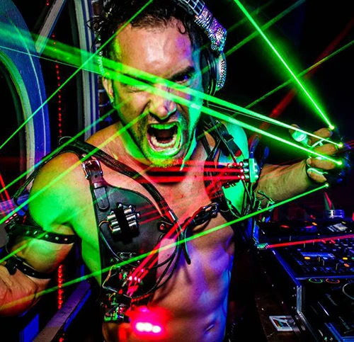 Energetic Kidd Madonny wearing leather straps and headphones, surrounded by green and red laser lights at a club.