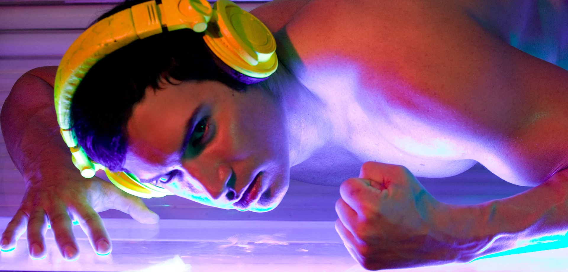 Kidd Madonny wearing yellow headphones with intense expression under purple and blue lighting.