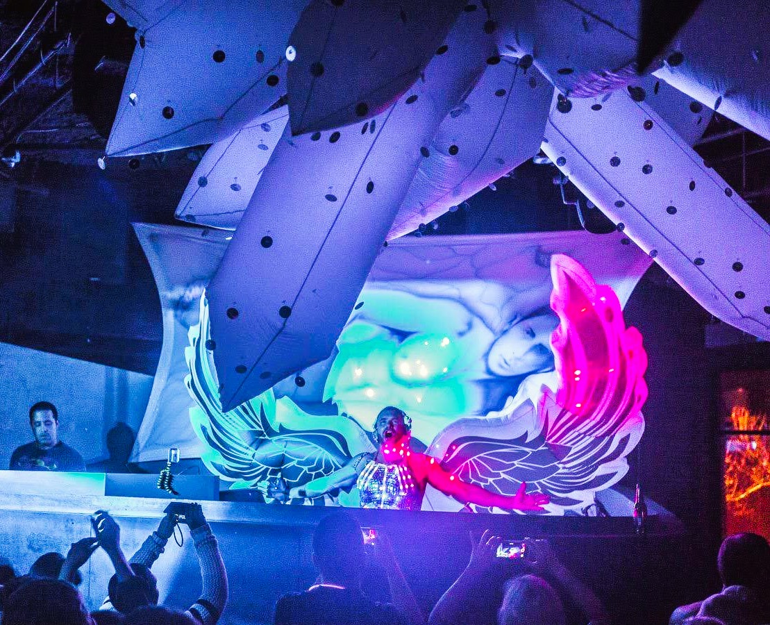 Kidd Madonny performing on stage with glowing angel wings and a crowd taking photos in front.
