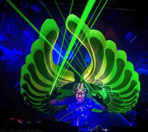 Kidd Madonny with glowing green inflatable wings and silver mask under green laser lights on a dark stage.