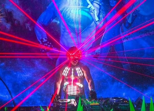 Kidd Madonny performing with red laser lights and neon body paint against a blue superhero mural background.