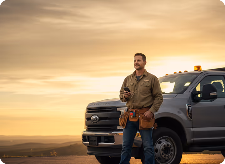 Contractor standing by his truck at sunset, phone in hand