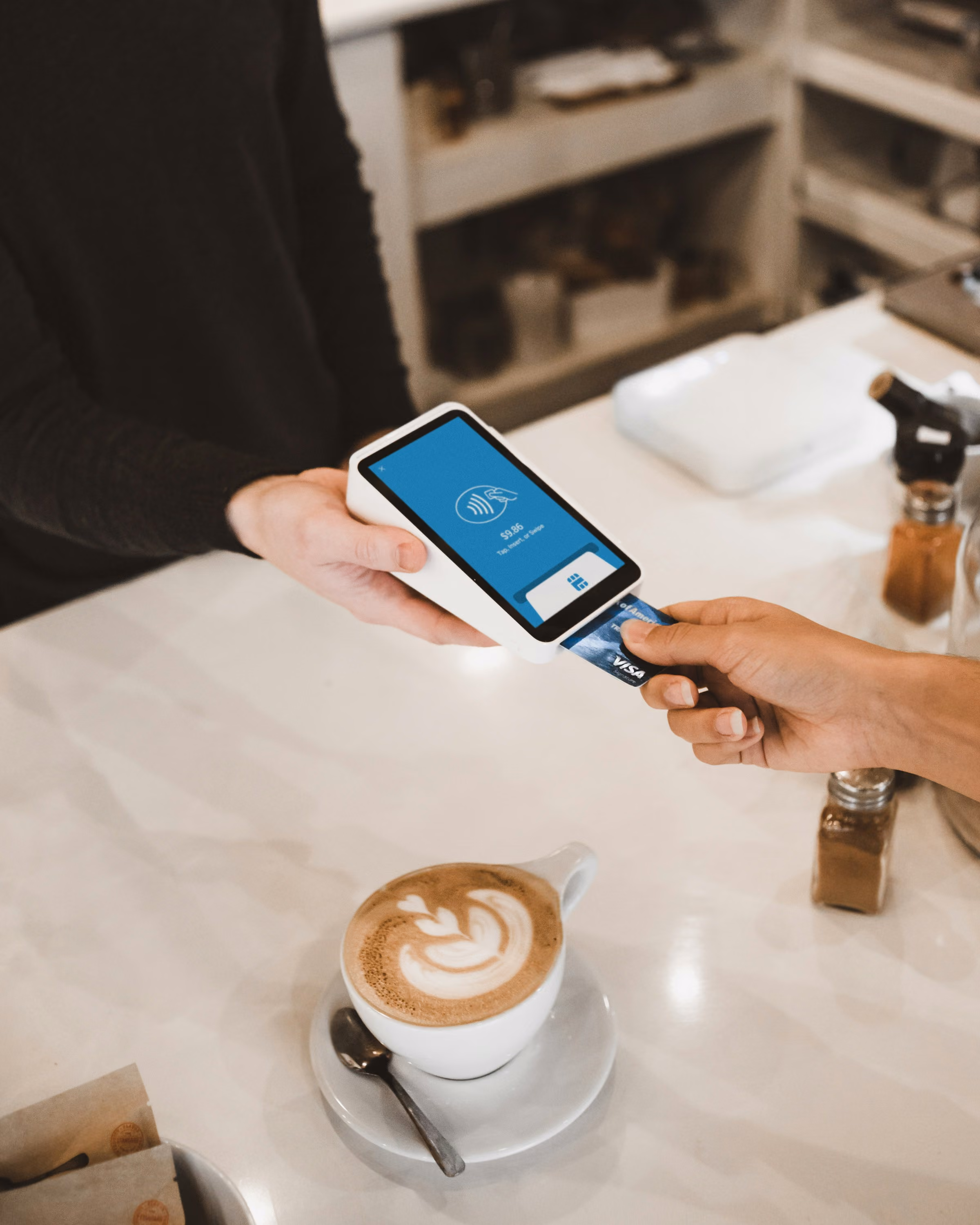 Customer paying with a Visa card on a mobile payment device at a cafe counter with a cup of coffee.