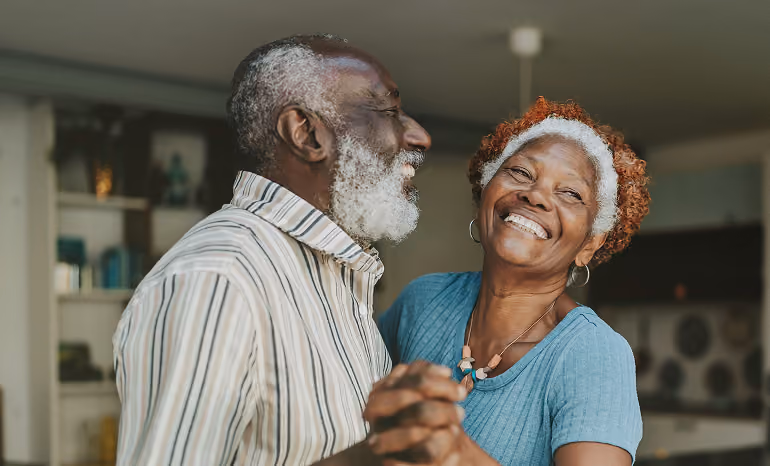 Smiling elderly couple dancing together indoors, holding hands and enjoying a happy moment.