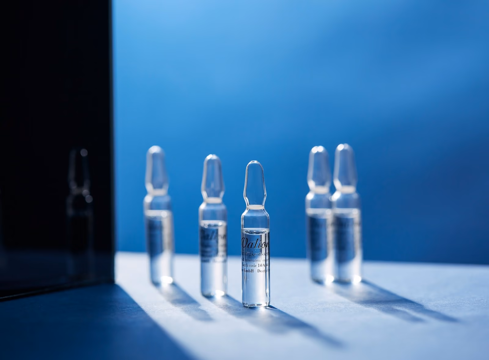 Row of clear glass peptide ampoules standing upright on a lit surface against a blue background
