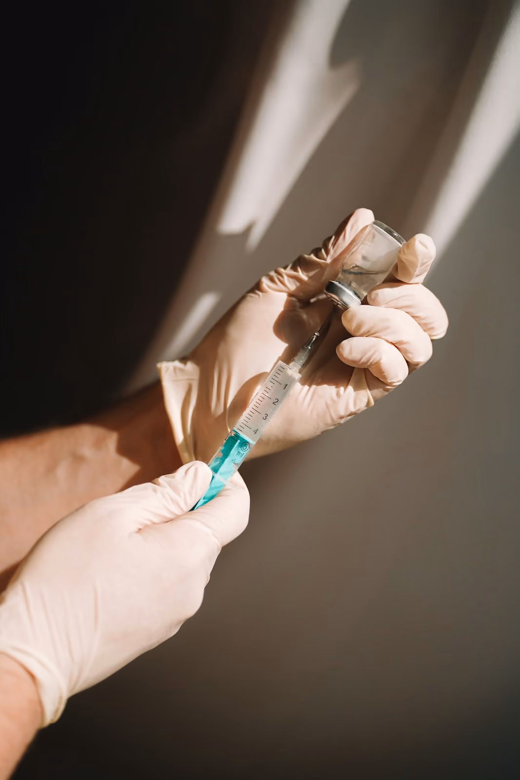 Gloved hands drawing a teal-colored solution from a small vial into a syringe
