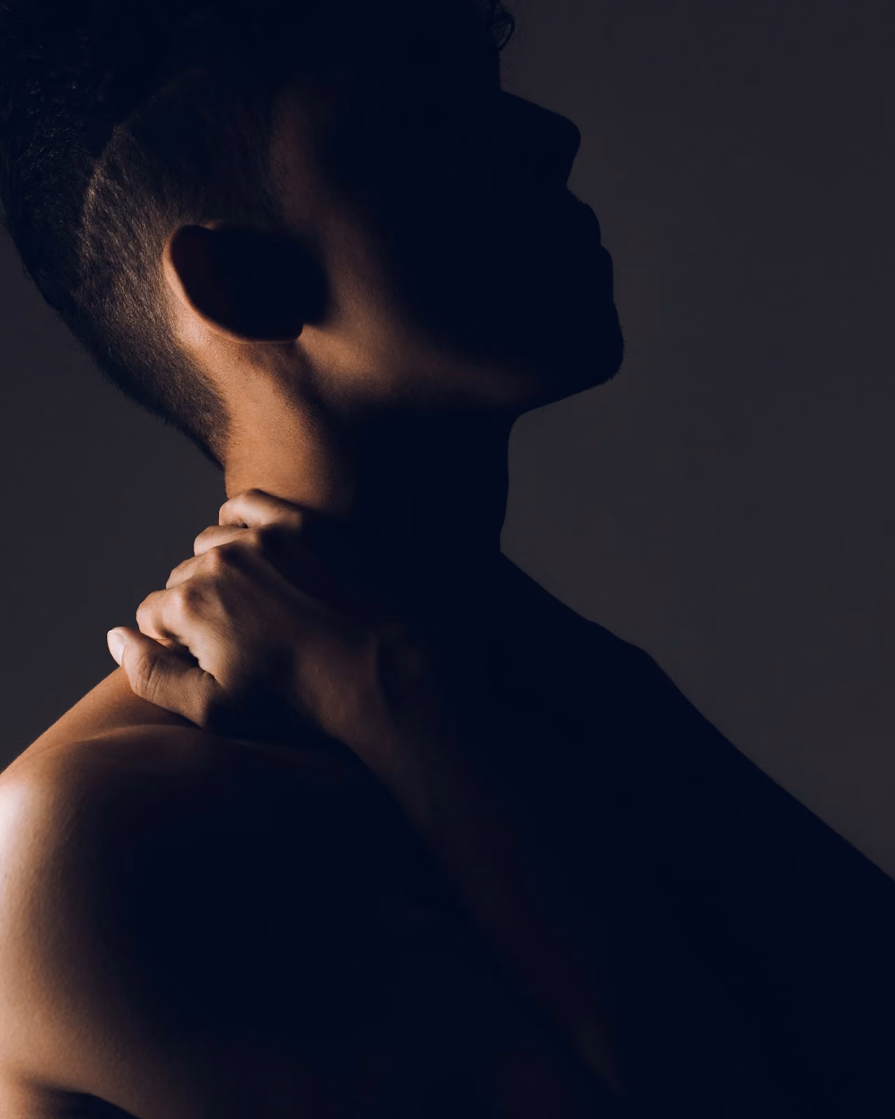 Silhouette of a shirtless man in profile gripping the back of his neck in discomfort