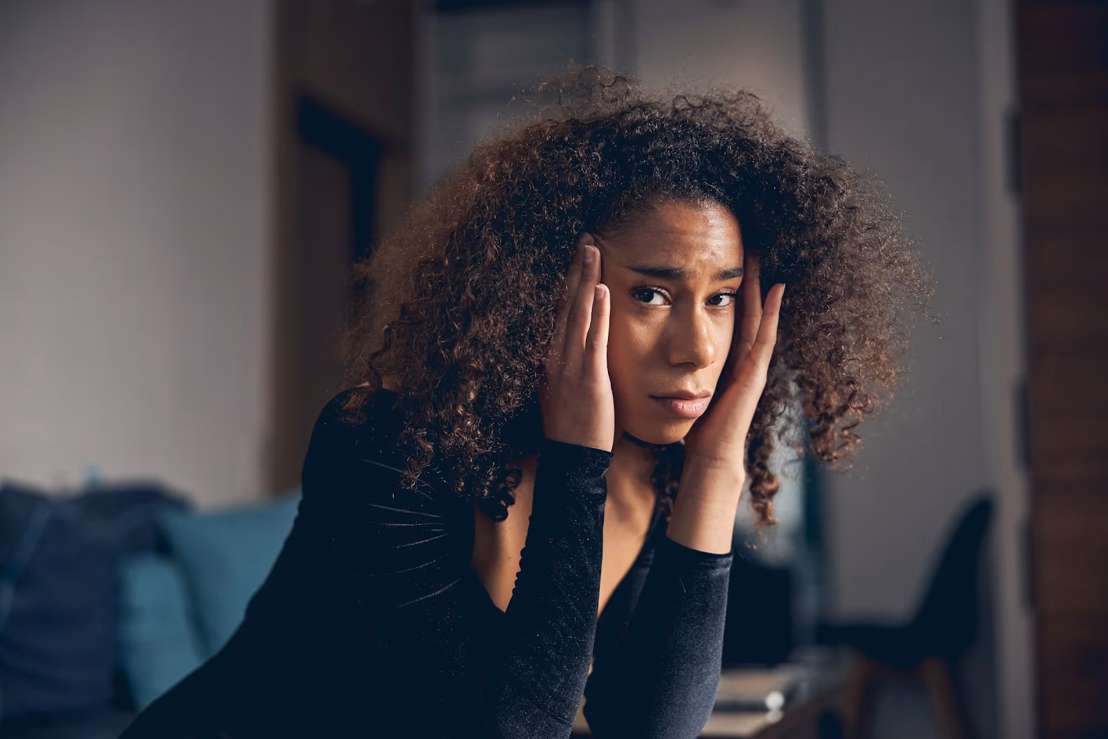Woman with curly hair pressing her hands to her temples, looking fatigued and stressed