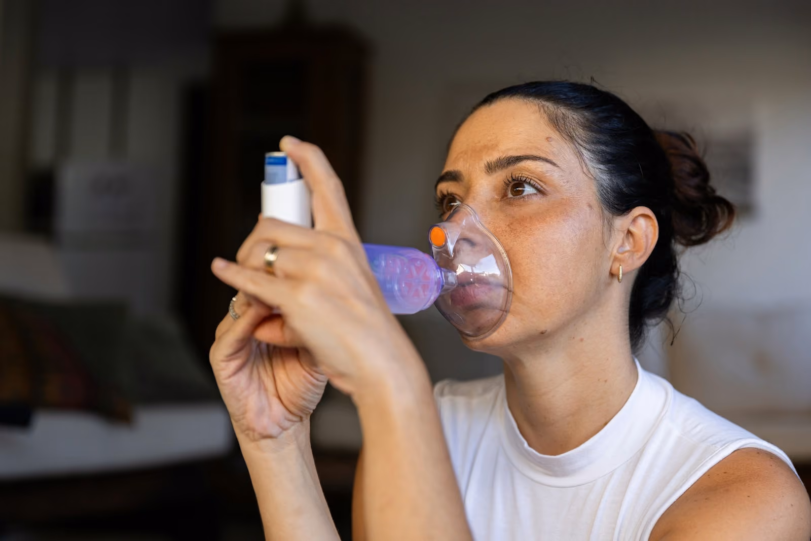 Woman using a handheld nebulizer mask to inhale medication at home
