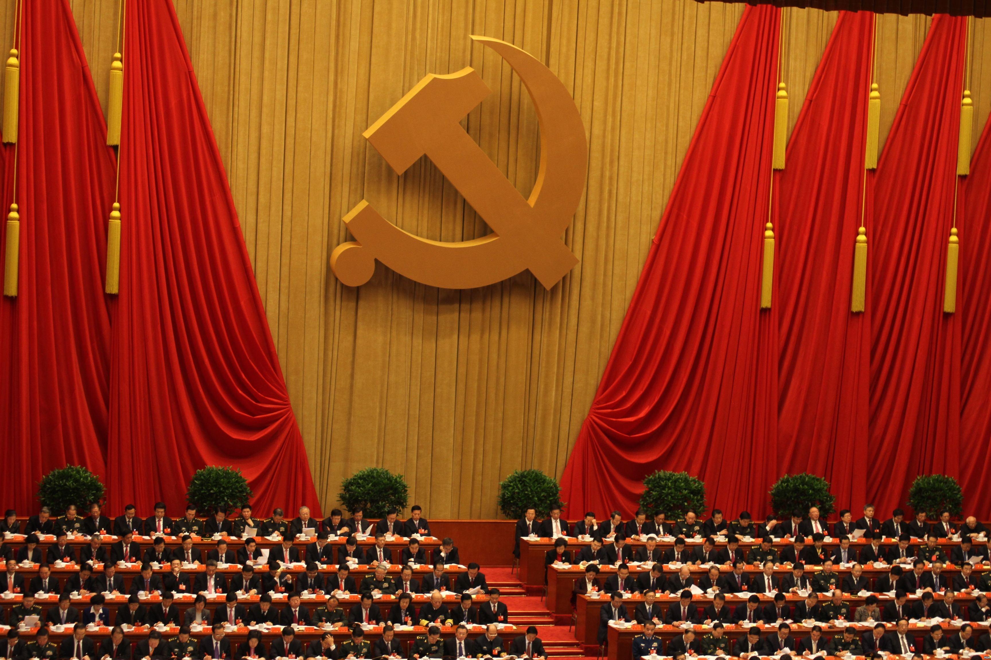 Chinese officials seated beneath a large hammer-and-sickle emblem at a Communist Party assembly.