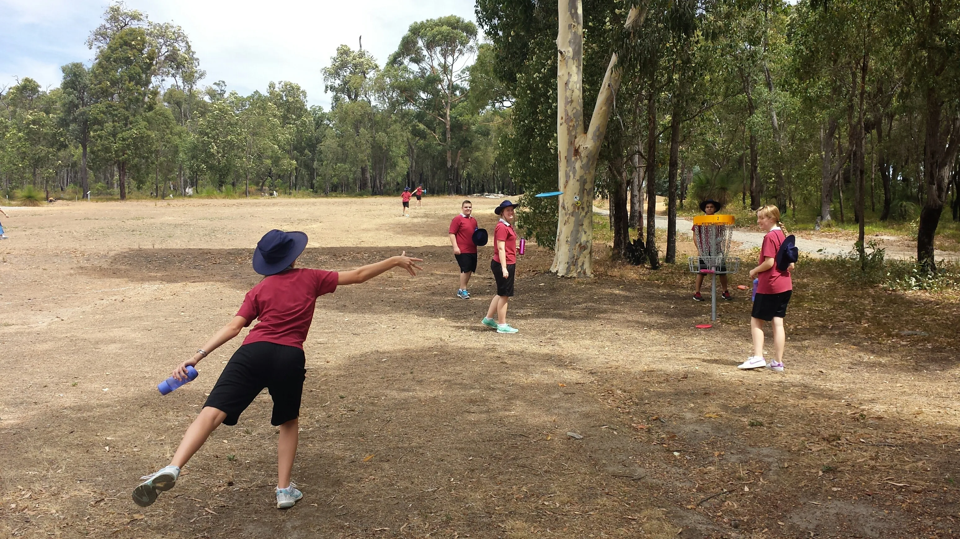 School students in maroon uniforms throwing discs toward a basket on a bush course