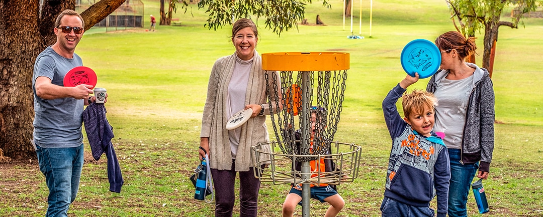 Families playing disc golf in a park