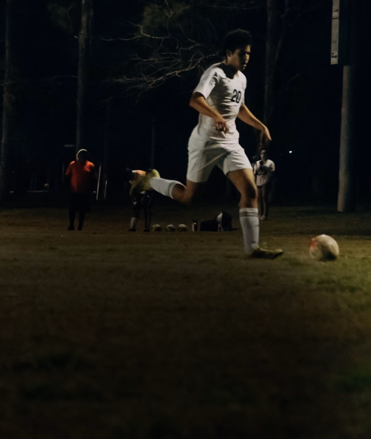 Footballer running with the ball on a floodlit pitch at night